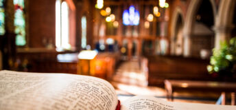 Bible open at the book of John inside an Anglican Church of England church. The focus is on the foreground of the bible, while in the background, defocused, are the pews and arches of the historic eighteenth century building. Horizontal colour image with copy space.