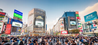 Panorama Shot of People crossing the crowded famous Shibuya Crossing in Downtown Tokyo, illuminated Shibuya Buildings with billboards in the background. Twilight light, close to sunset. Shibuya Crossing, Shibuya Ward, Tokyo, Japan, Asia.