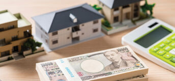 A photo of a desk with a calculator, model homes and a stack of yen bills.